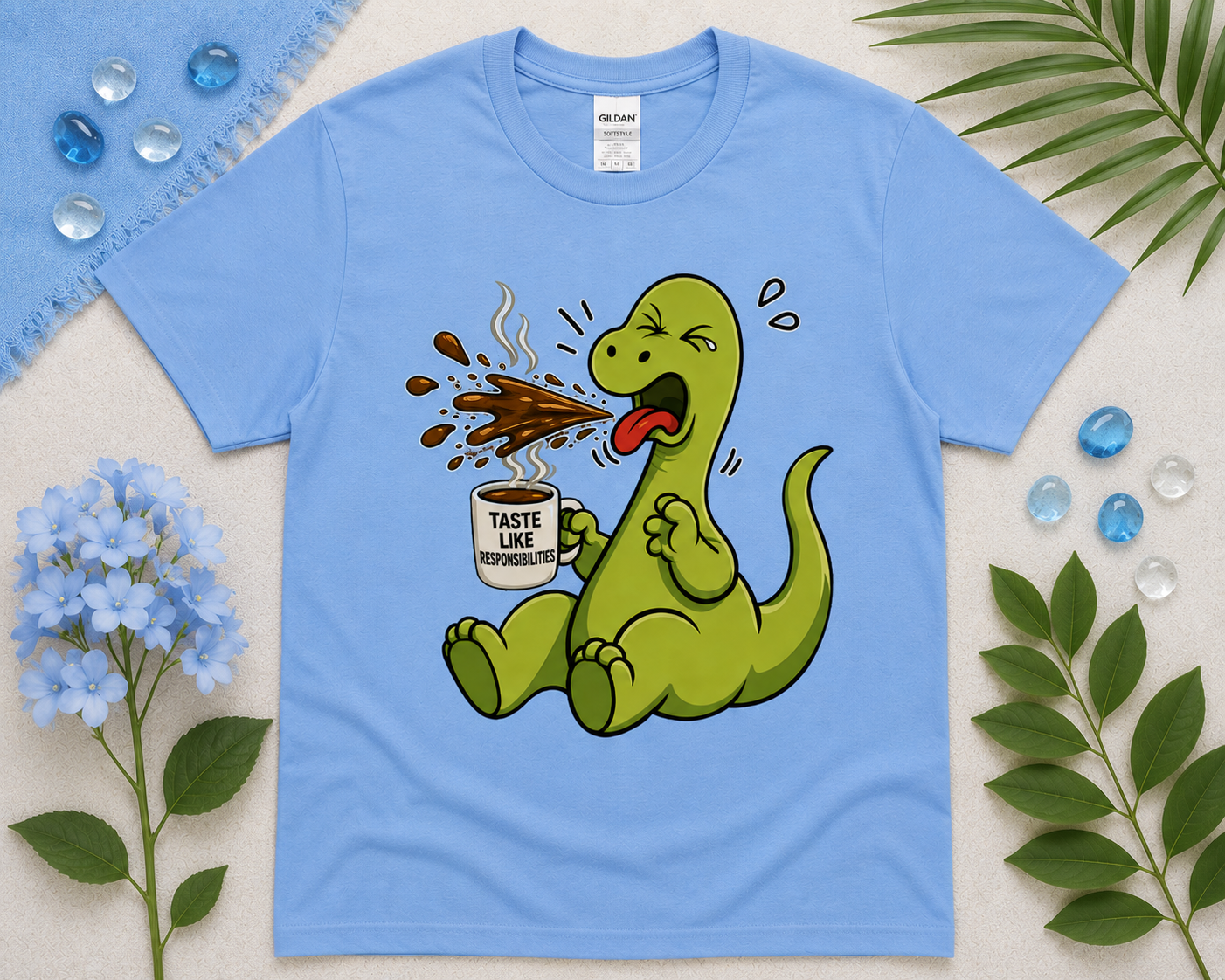 Funny dinosaur coffee graphic tee on Carolina blue Gildan shirt with cute caffeinated dino artwork and cozy pastel flat lay