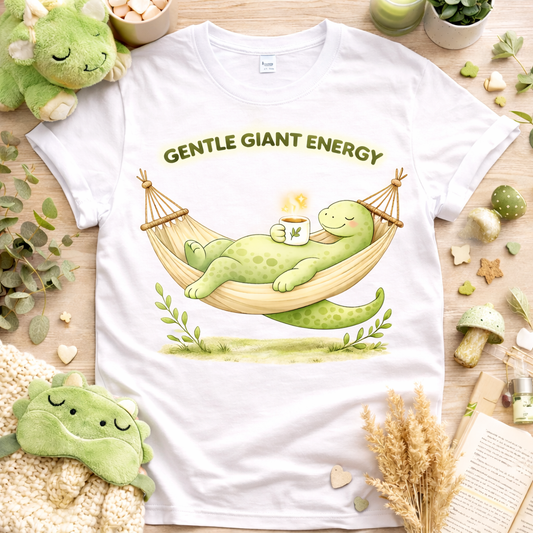 White shirt flatlay featuring a gentle giant energy brontosaurus relaxing in a hammock with cozy self care aesthetic props soft dinosaur graphic tee
