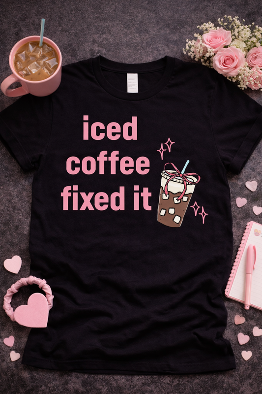 Black graphic t-shirt with pink text “iced coffee fixed it” and cute iced coffee illustration, styled in aesthetic flat lay with roses, iced coffee drink, and pink accessories