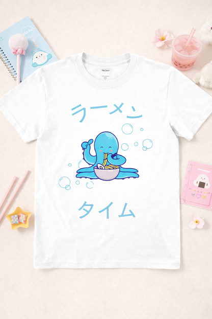 White graphic t-shirt featuring kawaii octopus eating ramen with Japanese text and bubbles, styled in a pastel flatlay with cute accessories and soft aesthetic props