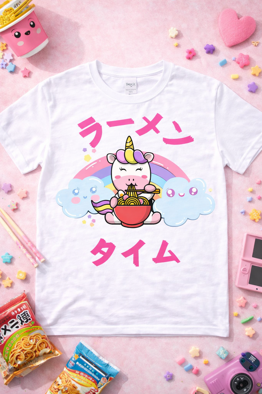 White graphic t-shirt featuring kawaii unicorn eating ramen with rainbow and Japanese text, styled in a cute pastel flatlay with snacks and playful accessories