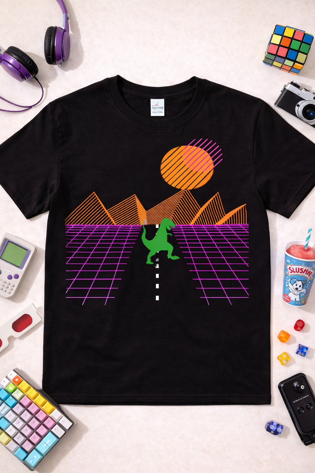 Black graphic t-shirt featuring neon T-Rex retro sunset design with synthwave grid landscape, styled in a flatlay with colorful 80s accessories and gaming props
