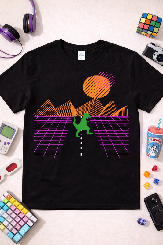 Black graphic t-shirt featuring neon T-Rex retro sunset design with synthwave grid landscape, styled in a flatlay with colorful 80s accessories and gaming props