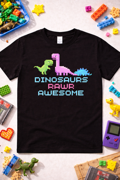 Black graphic t-shirt featuring pixel dinosaurs and “Dinosaurs Rawr Awesome” text in 8-bit retro style, styled in a fun flatlay with retro toys and gaming props