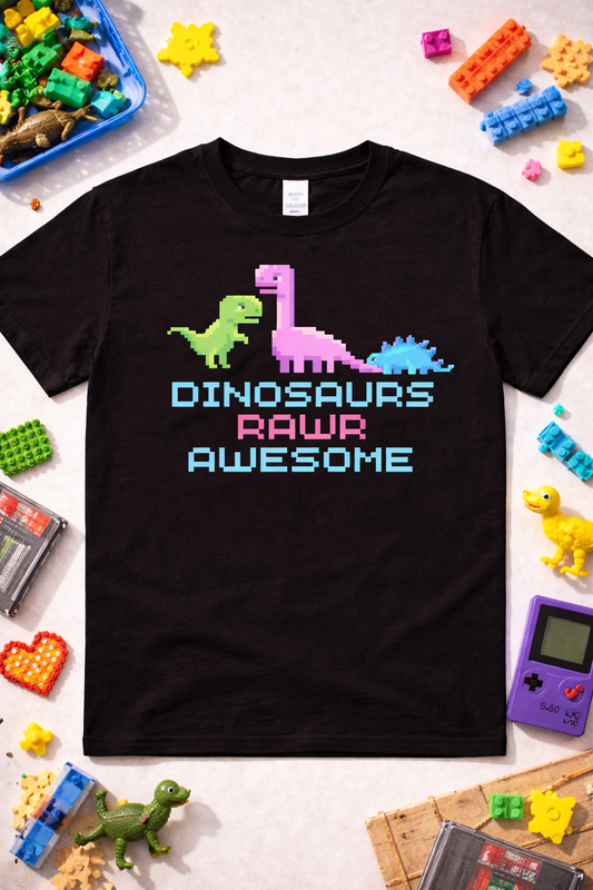 Black graphic t-shirt featuring pixel dinosaurs and “Dinosaurs Rawr Awesome” text in 8-bit retro style, styled in a fun flatlay with retro toys and gaming props