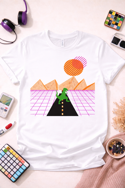 White graphic t-shirt featuring neon vaporwave T-Rex walking on black road with retro sunset, grid mountains, and 80s aesthetic styled in flat lay with colorful props