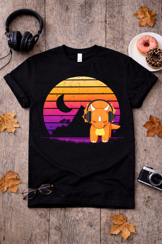 Black graphic t-shirt featuring a retro triceratops dinosaur with headphones and sunset design, styled in a flatlay with fall leaves, donuts, camera, and cozy aesthetic props