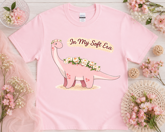 Soft Era Bloom Brontosaurus graphic tee on light pink Gildan shirt with soft floral flatlay props