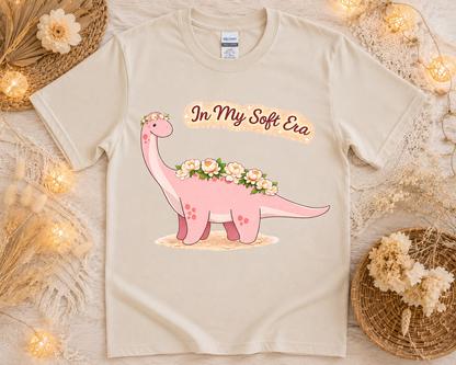 Cozy cottagecore dinosaur graphic tee on sand Gildan shirt with soft floral aesthetic props