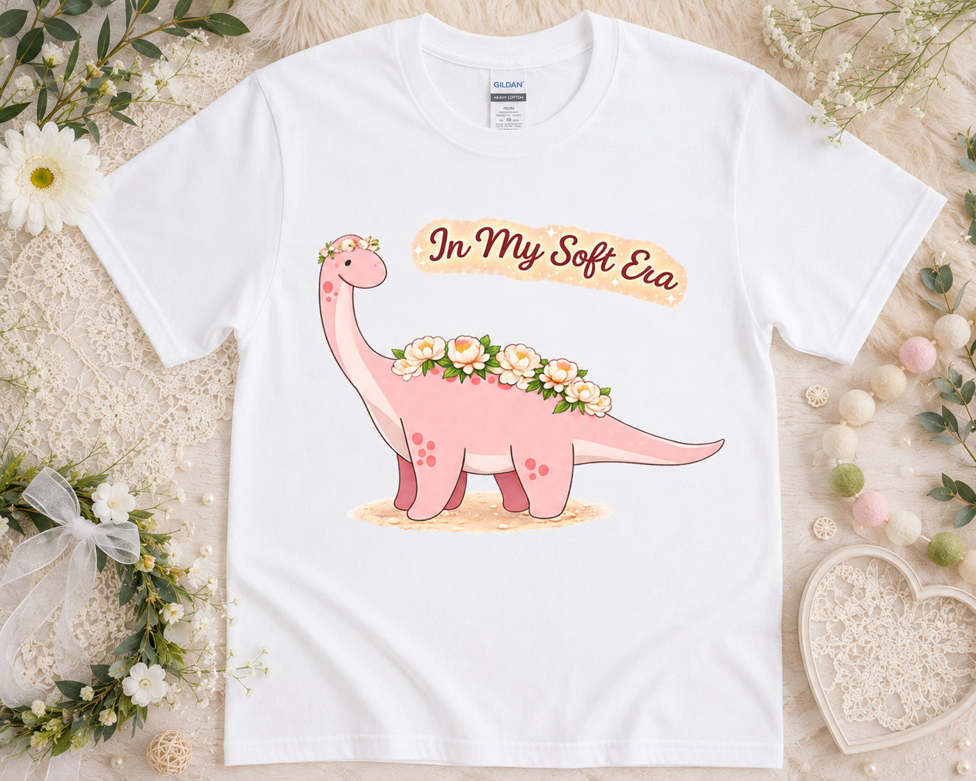 In My Soft Era pink brontosaurus graphic tee on white Gildan shirt with feminine floral props