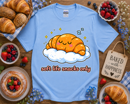 Pastel blue kawaii bakery shirt with sleepy croissant cloud graphic and soft life snacks only phrase on Carolina blue Gildan 5000 styled with fresh baked bakery props for trendy women teen girls and dessert lovers in the United States