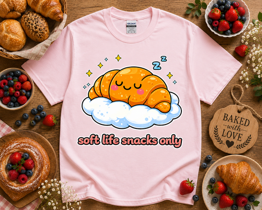 Cute kawaii croissant bakery graphic tee on light pink Gildan 5000 shirt with soft life snacks only design flat lay styled with pastries berries and cozy bakery aesthetic perfect for women teen girls and foodie gift shoppers in Los Angeles California