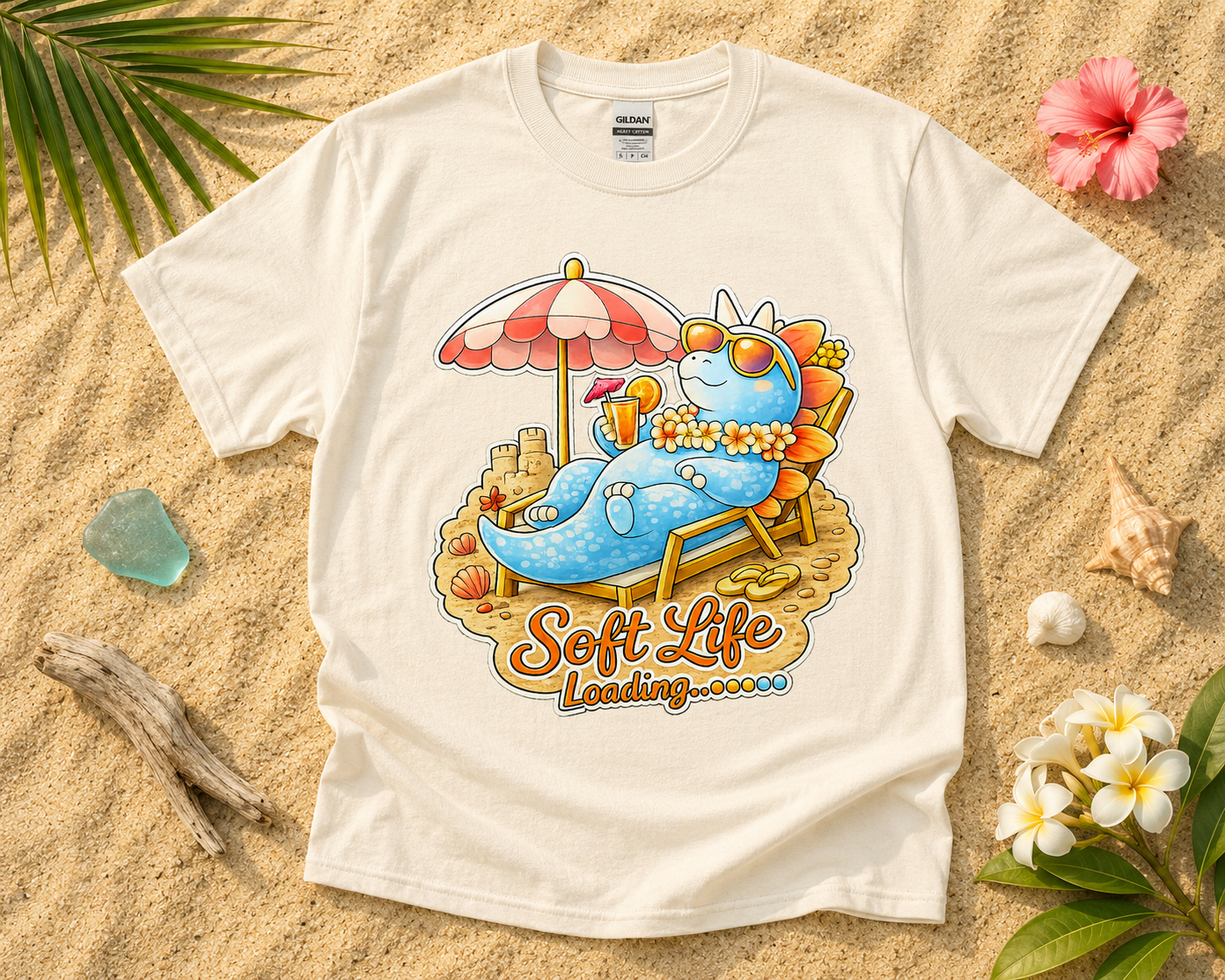 Soft Life Stegosaurus dinosaur graphic tee on natural Gildan shirt with beach sand tropical vacation flatlay cozy summer aesthetic